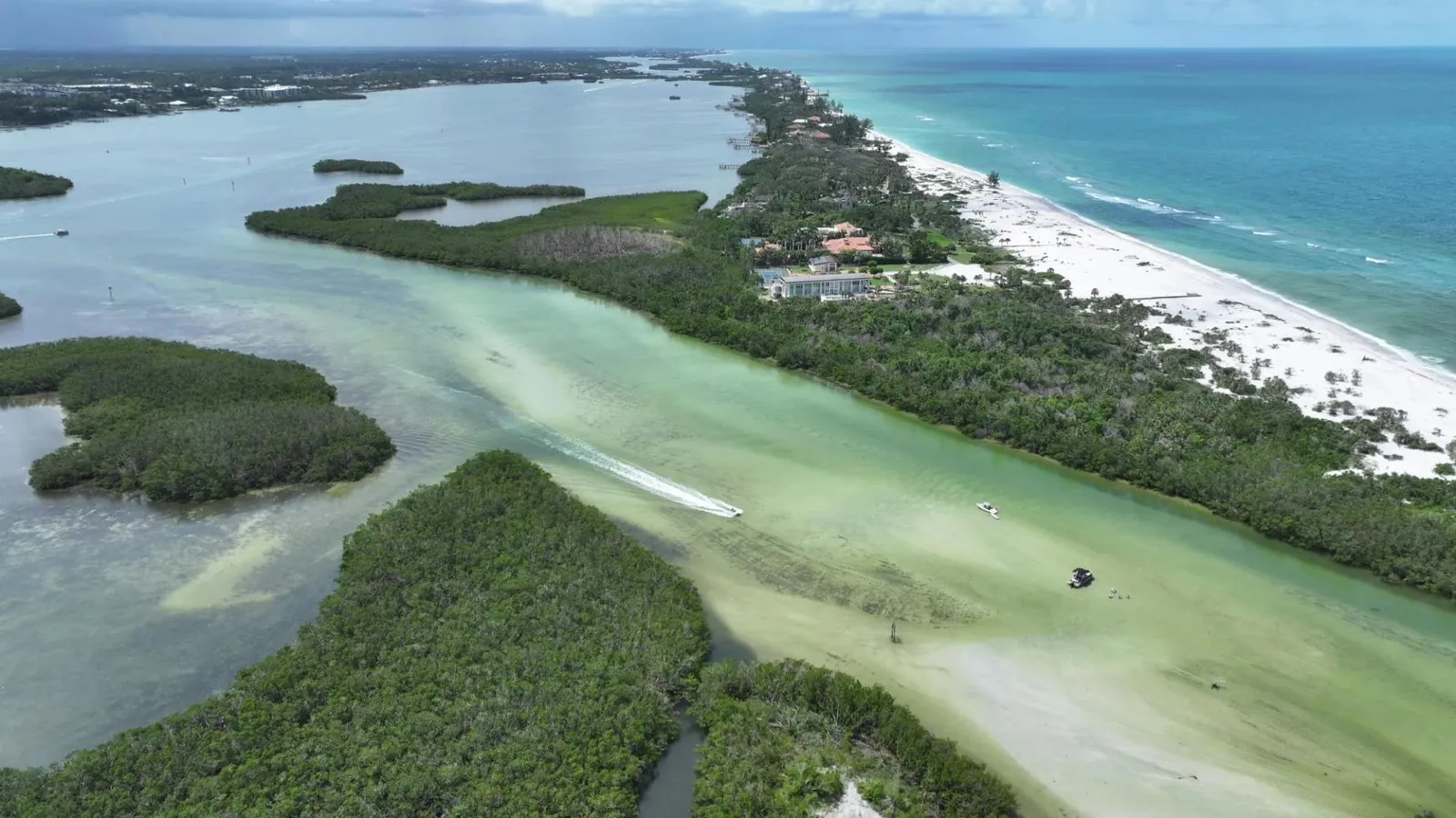 Aerial view of Midnight Pass: a boat crossing the clear green inlet between mangrove islands, with Siesta Key's white beach and the Gulf beyond
